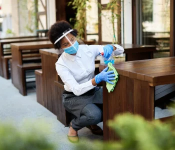 African American waitress disinfecting tables at outdoor cafe during coronavirus epidemic.